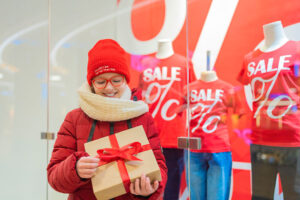 Woman with a Christmas gift outside a retail store window advertising sales