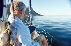 A man looking at a tablet while relaxing on a sailboat.