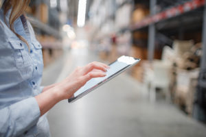 Image of a woman using a tablet in a warehouse aisle.
