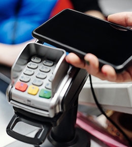 Touchless payments - Hand holding cell phone over a retail payment terminal.
