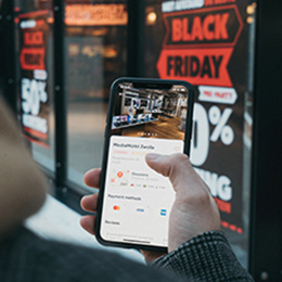 Man looking at a cell phone screen outside a store with a Black Friday sale