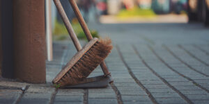 A broom and dustpan leaning against a storefront on a cobblestone sidewalk.
