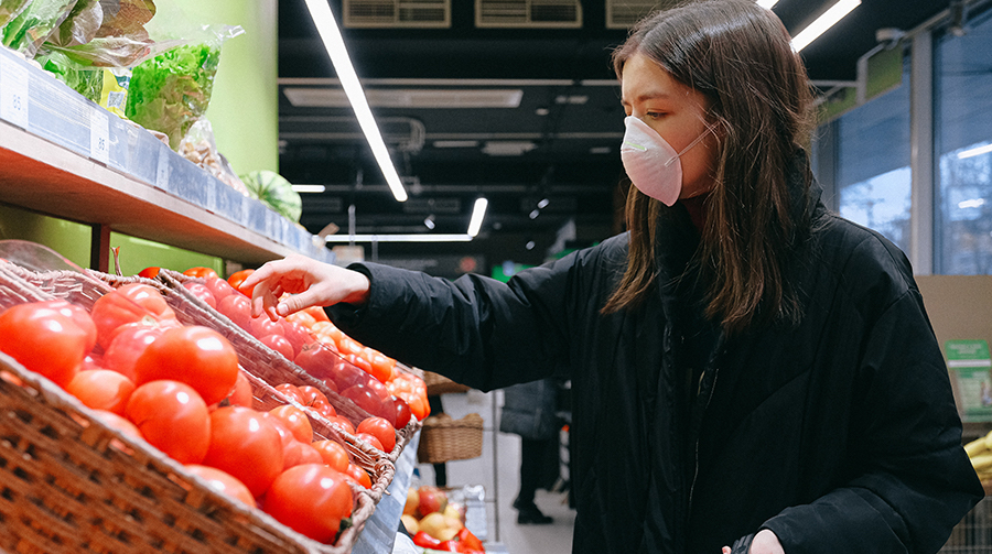 Woman in face mask reaching for tomato display in grocery store