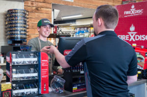 Smiling young man standing behind cash register hands customer credit card
