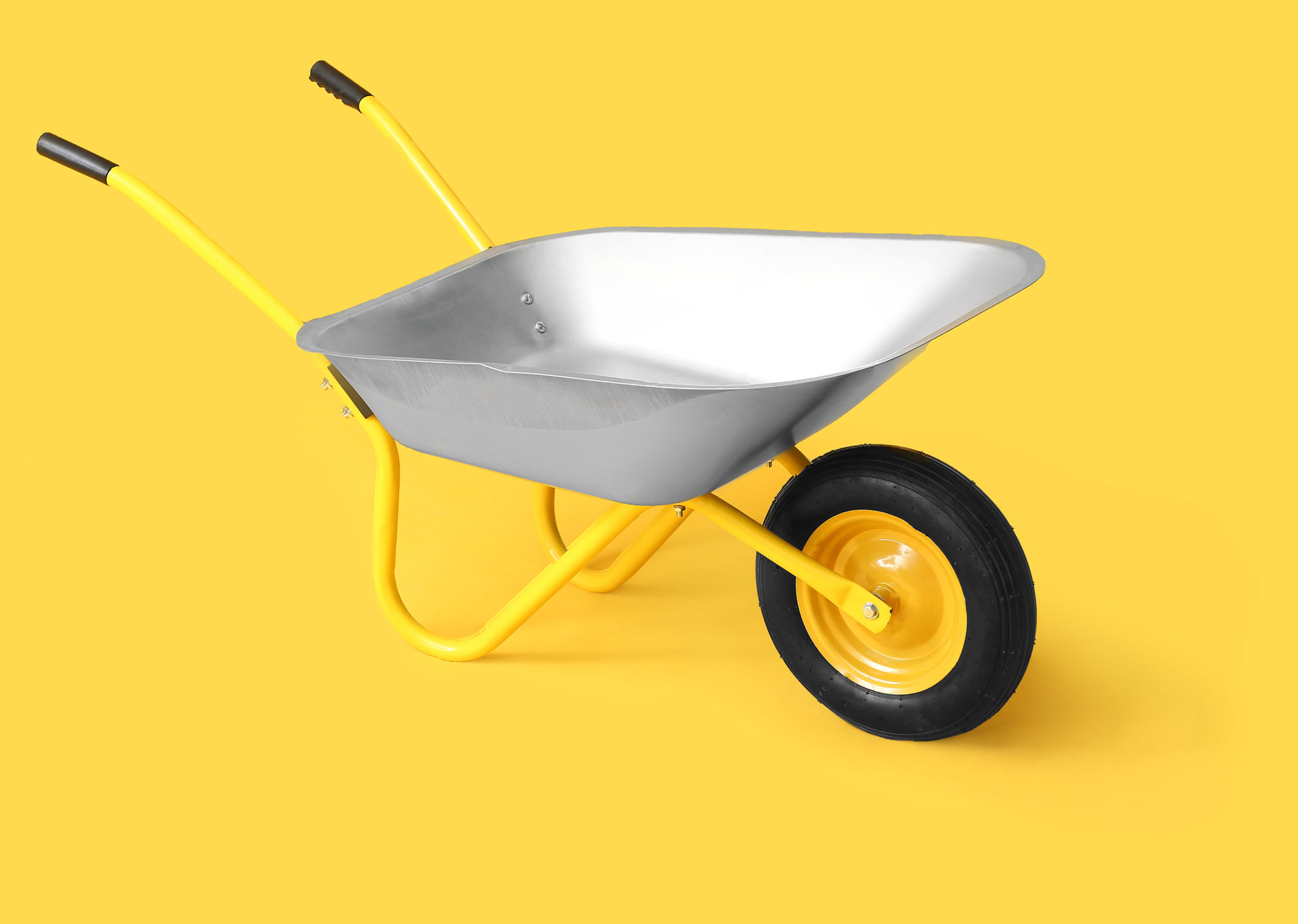 A wheelbarrow with yellow handles sits on a yellow backdrop