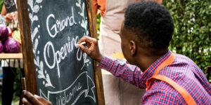 Image of a business owner writing "Grand Opening" on a sandwich board