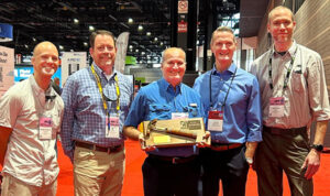 Crossroads owners Joe Rush, right, Drew Atchison, far left, joins former store owner Tim Gibson, in Chicago for Ace’s 100th anniversary last June. There, Ace President and CEO John Venhuizen presented John with the Golden Hammer Award from Estwing Manufacturing.